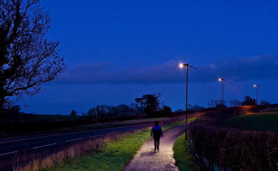 man walking on pathway lit by solar lighting